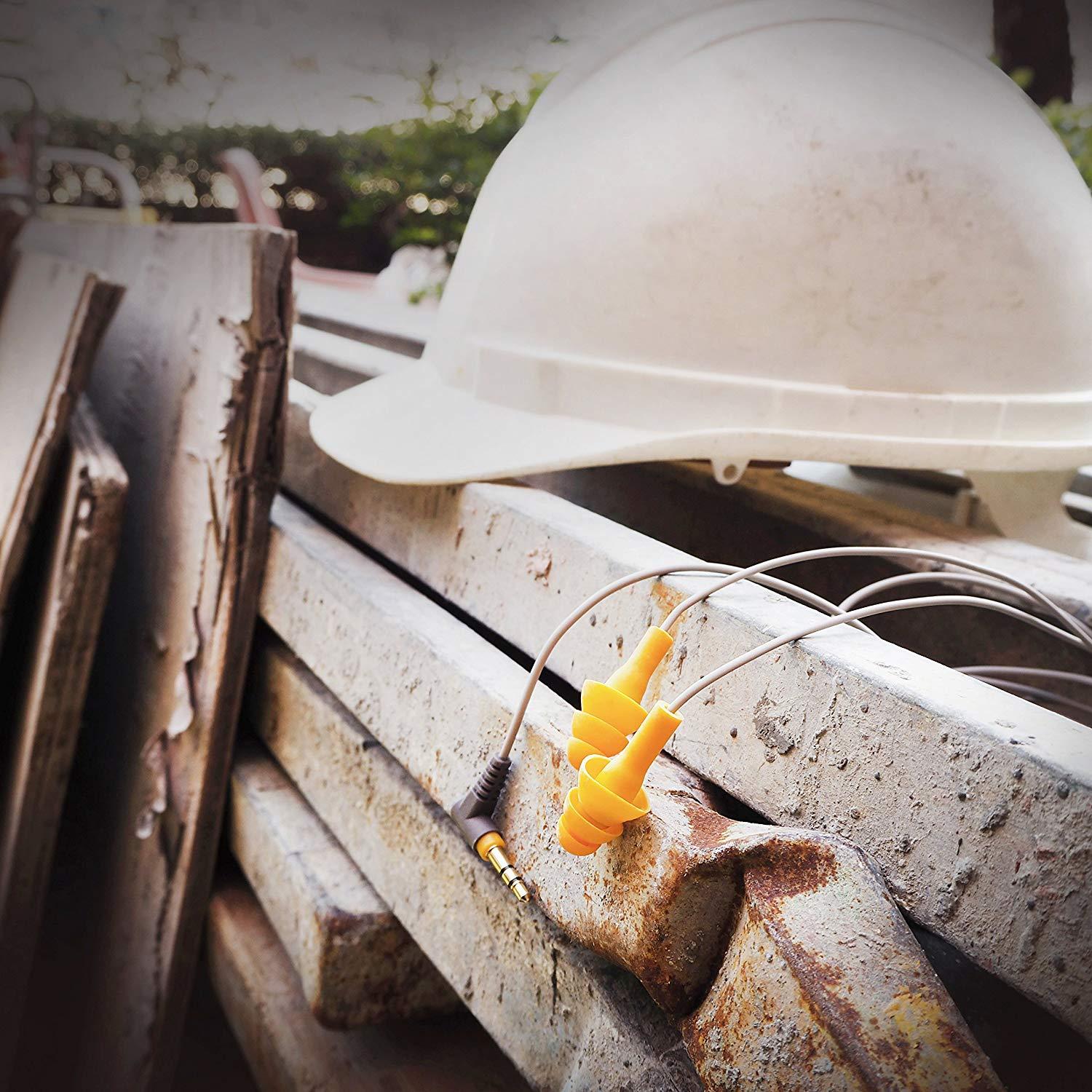 An image of the Elgin Ruckus Earplug Earphone laying on a pile of lumber next to a construction hat at a worksite.